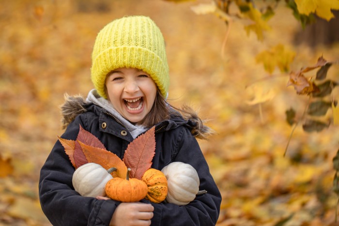 little funny girl yellow hat with small pumpkins autumn forest blurred background copy space